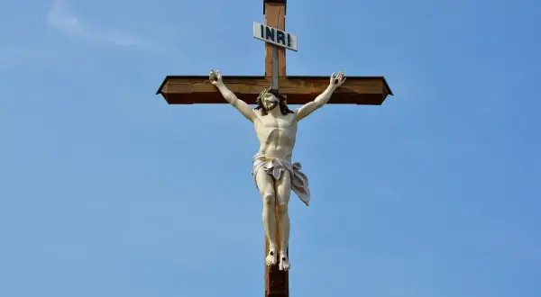 Figurka Jezusa na drewnianym krzyżu pod błękitnym niebem.