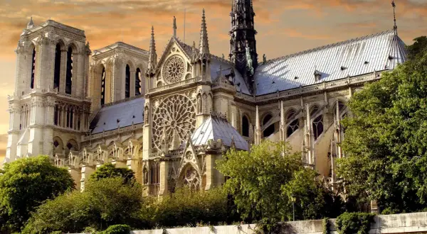 Katedra Notre Dame w Paryżu z różanymi oknami i wieżami na tle pomarańczowego nieba.