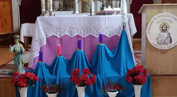 Ołtarz kościelny udekorowany na adwent: świece, kwiaty i figurka.